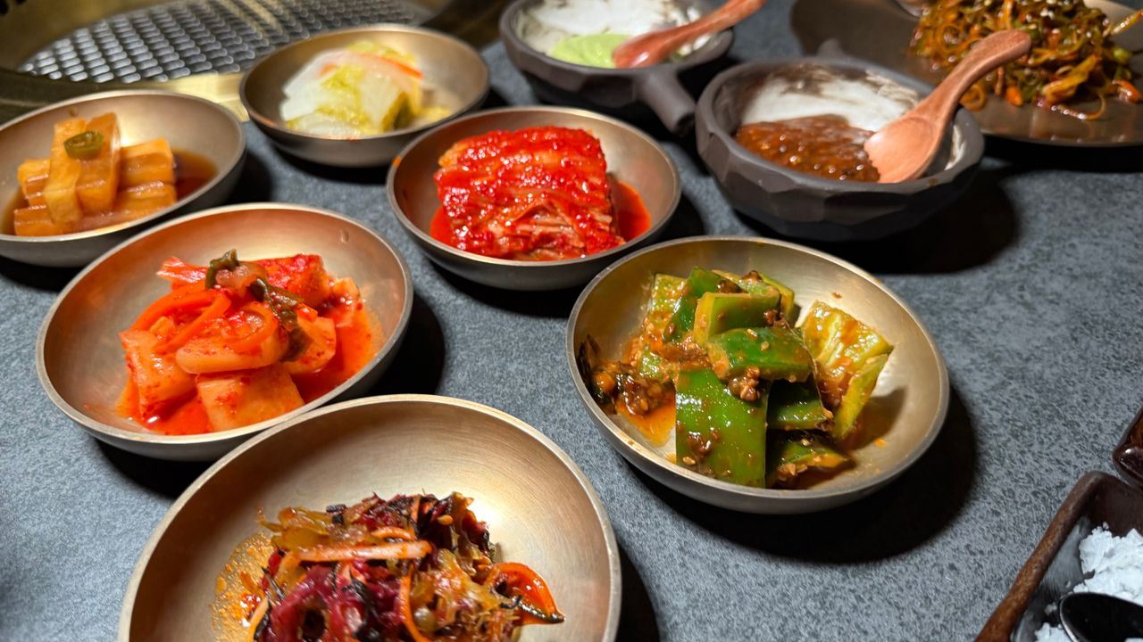 Variety of Korean banchan side dishes served in metallic bowls on a table.